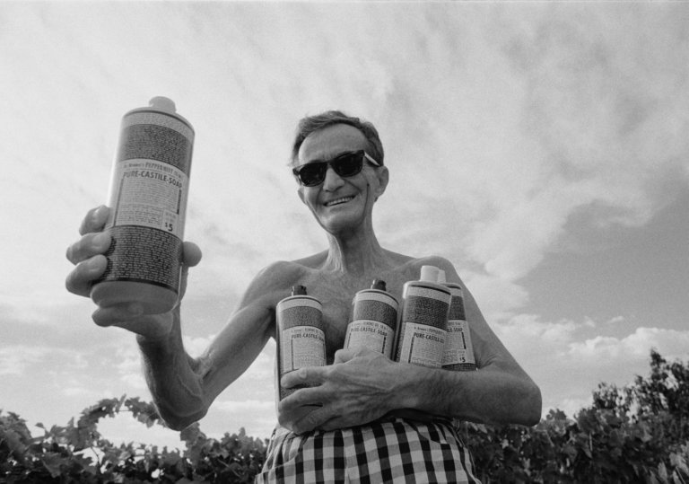 a skinny white man in sunglasses holding four bottles of liquid soap